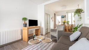 Una sala de estar moderna con un sofá, un televisor, un escritorio de madera y un comedor con una mesa y sillas.