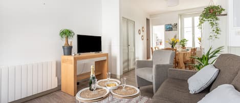 A modern living room with a sofa, a TV, a wooden desk, and a dining area with a table and chairs.