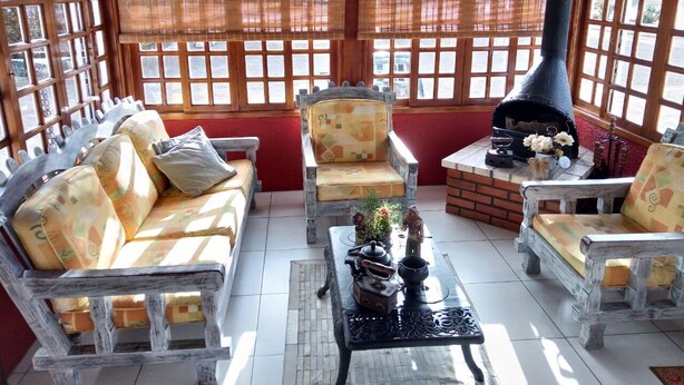 A cozy room with wooden furniture, a brick fireplace, and large windows. - Hotel Pequenino (Canela)