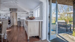 Une cuisine moderne avec des meubles en bois, un coin repas avec des chaises en osier et une vue sur le jardin grâce à une porte vitrée.