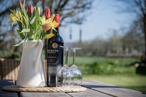 Una bottiglia di vino, due bicchieri da vino e un vaso con fiori su un tavolo all'aperto.