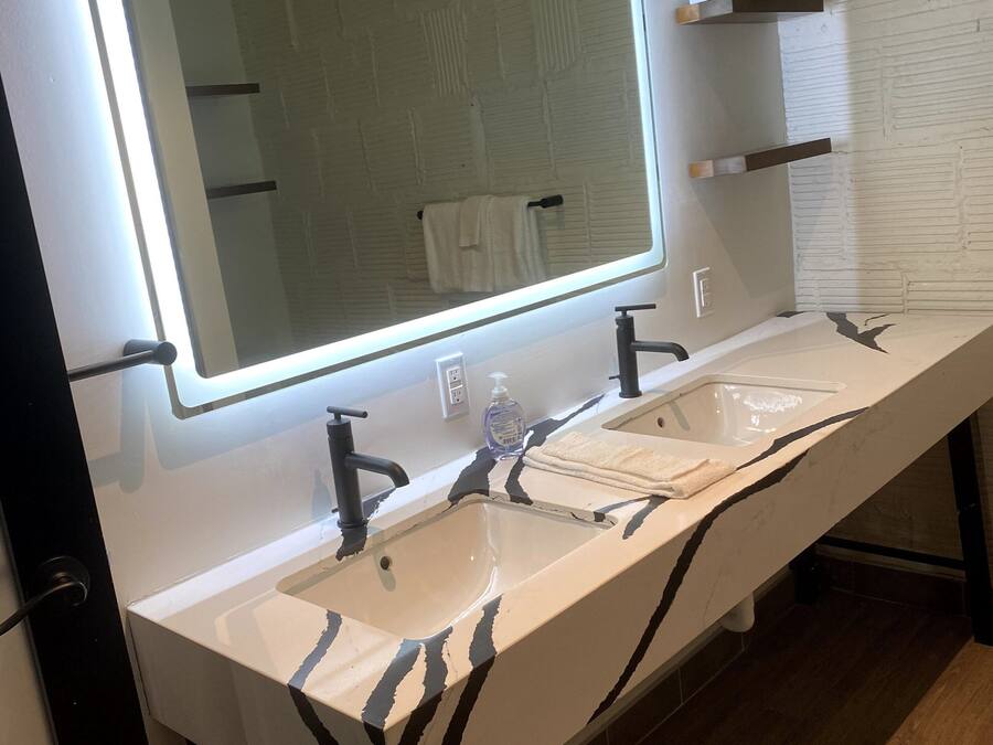 Une salle de bain dotée d’un long meuble-lavabo, de deux vasques, d’un miroir avec éclairage indirect et d’un porte-serviettes.
