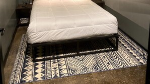 A neatly made bed with a white comforter and pillows, a patterned rug, a wall-mounted TV, and a small bedside table with a lamp. - 424 Gold Way-Apt 402, 2 Bed/1Bath (Pittsburgh)