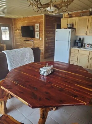 A wooden dining table with a built-in radio, a kitchen area with wooden cabinets, a refrigerator, and a television mounted on the wall. - Cedar River Retreat & Hideaway (Ericson)