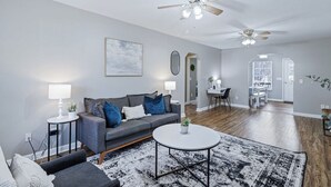 Ein modernes Wohnzimmer mit grauem Sofa, rundem Couchtisch und Deckenventilator.