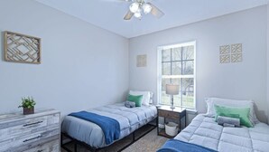 Ein Schlafzimmer mit zwei Betten, einem Schminktisch, einem Fenster mit Jalousien und einem Deckenventilator.
