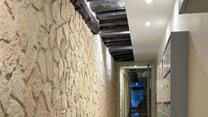 A hallway with textured stone walls, a tiled floor, and a staircase leading to another level. - Lovely studio for 3 in the heart of the Marais (Paris)