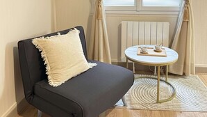 A small room with a black sofa, a round table, and a radiator. - Lovely studio for 3 in the heart of the Marais (Paris)