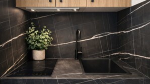 A modern kitchen with black marble tiles, a wooden cabinet, a black faucet, and a potted plant. - Lovely studio for 3 in the heart of the Marais (Paris)
