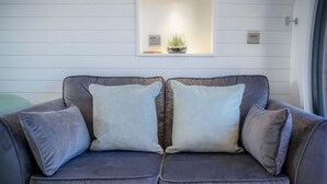 A grey sofa with two cushions and a small shelf above it. - Bracken Burrows - 1 Bedroom Pod - New Hedges (Tenby)