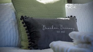 A bed with a pillow labeled "Bracken Burroughs EST 2022" and a green pillow. - Bracken Burrows - 1 Bedroom Pod - New Hedges (Tenby)