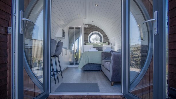 A cozy, circular room with a bed, seating area, and a window. - Bracken Burrows - 1 Bedroom Pod - New Hedges (Tenby)