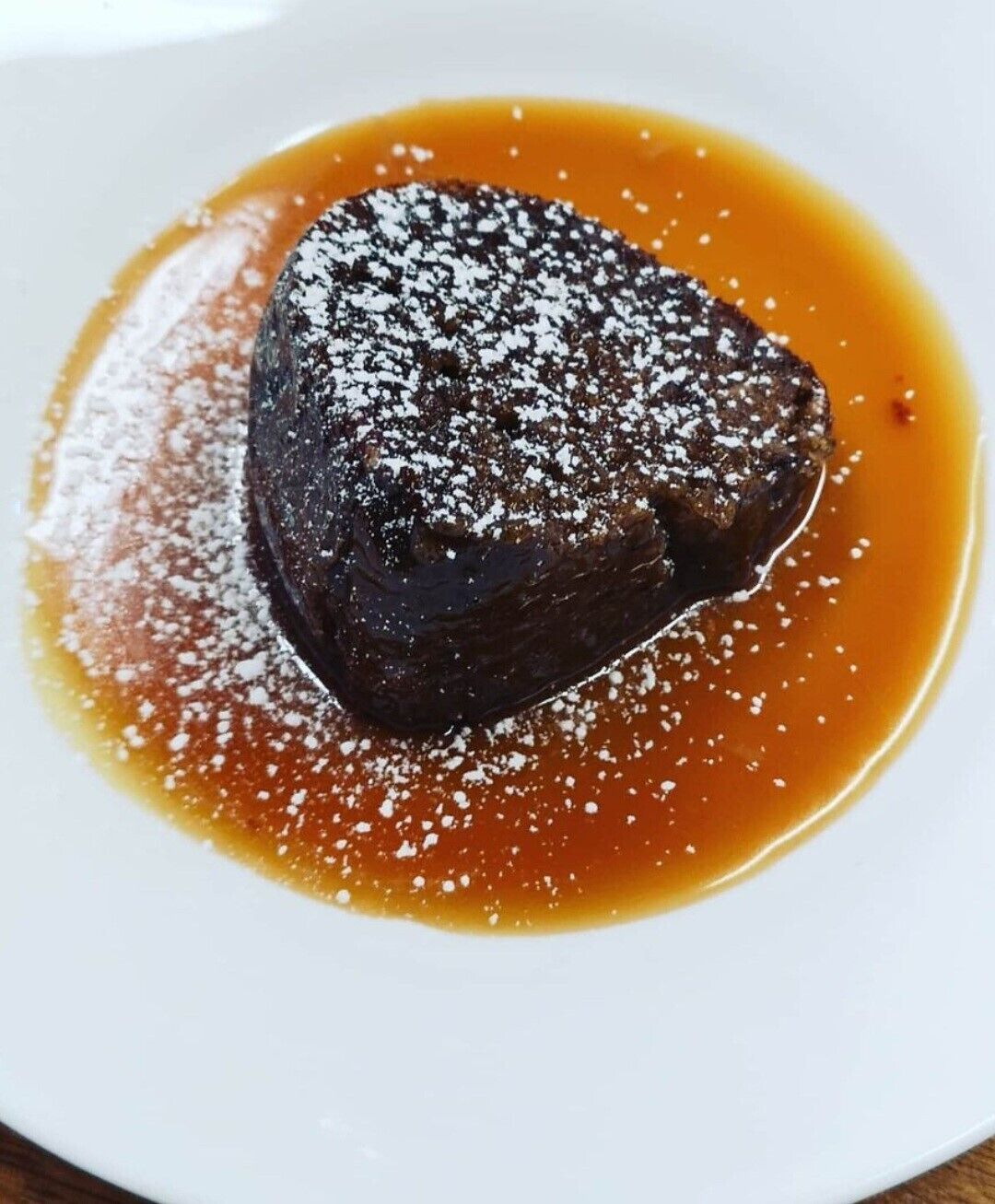 A dessert on a white plate with caramel sauce and powdered sugar.
