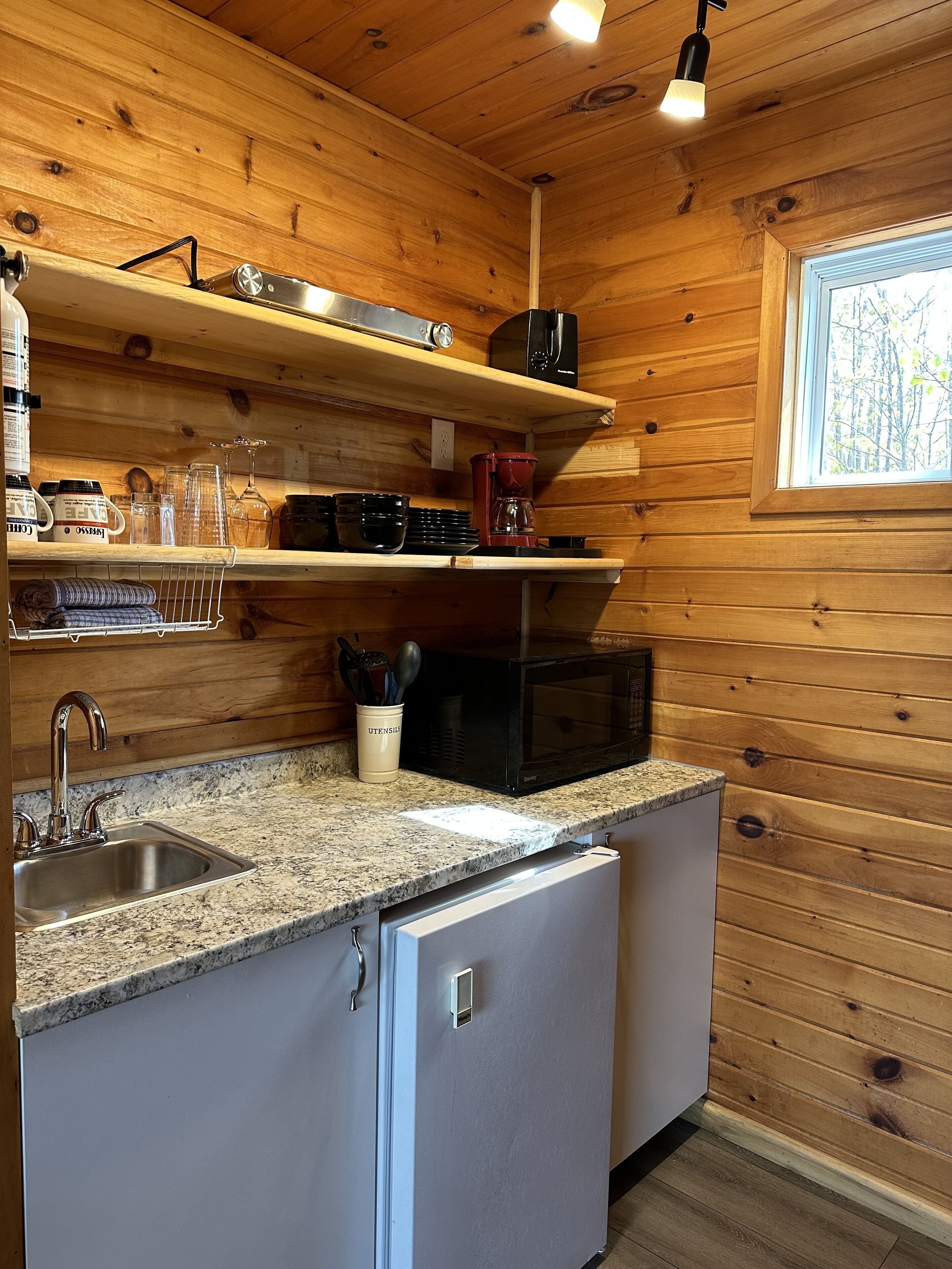 A compact kitchen with wooden walls, a granite countertop, a sink, a microwave, and a coffee maker.