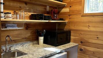 A compact kitchen with wooden walls, a granite countertop, a sink, a microwave, and a coffee maker.