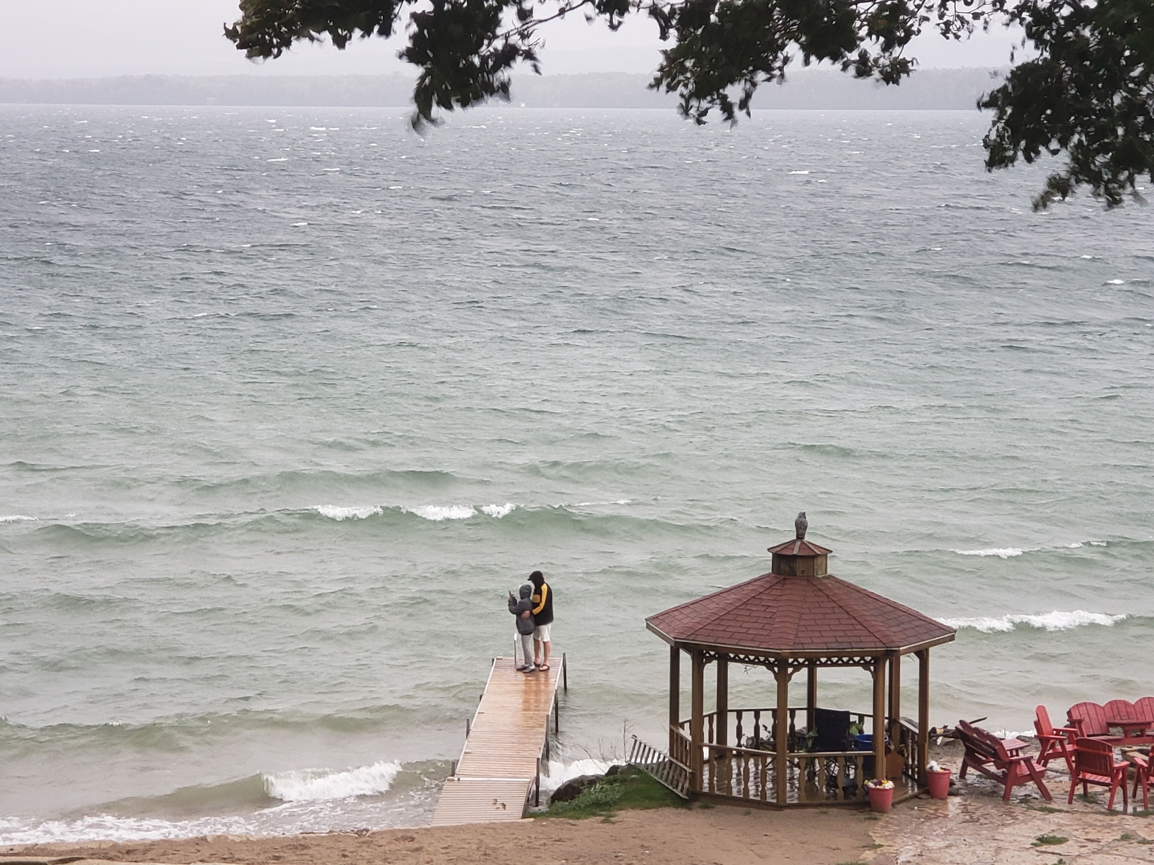 A wooden pier extending into a body of water with a gazebo and red chairs at the end.