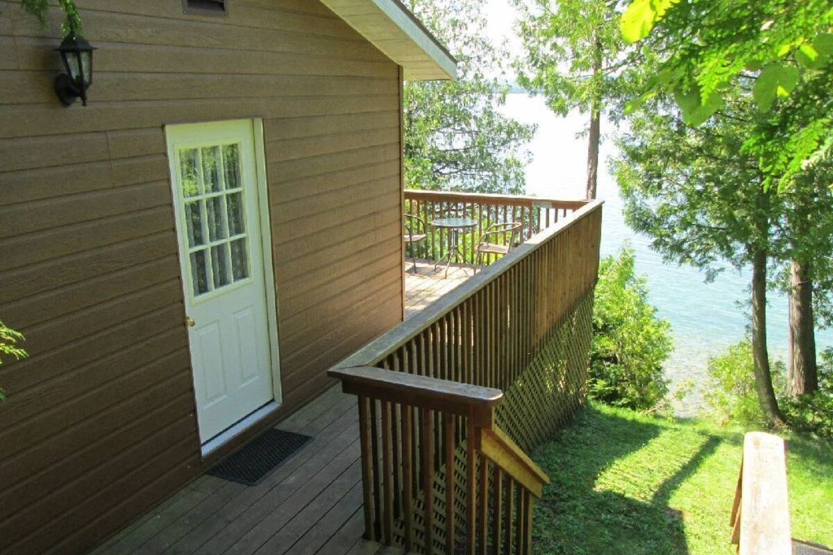 Une terrasse en bois avec une porte blanche, une petite table et des chaises, et une vue sur un lac.