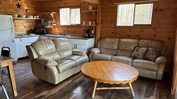 A cozy cabin interior with a wooden interior, a kitchenette, two leather sofas, and a round wooden table.