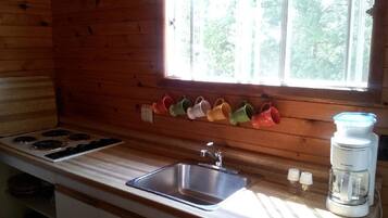 A kitchen with a wooden interior, a stainless steel sink, a stove, and a window with a view of trees.