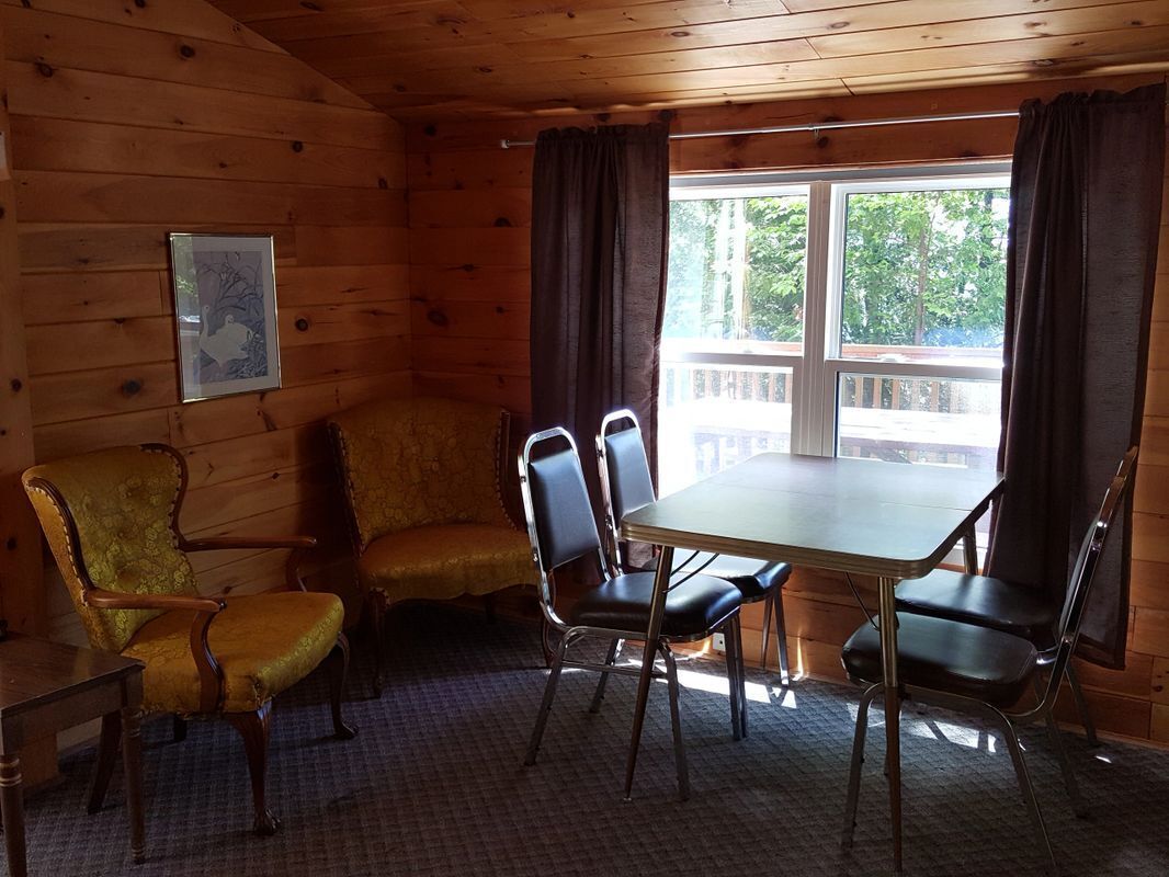 A wooden cabin room with a dining table and chairs, a sofa, and a framed picture on the wall.