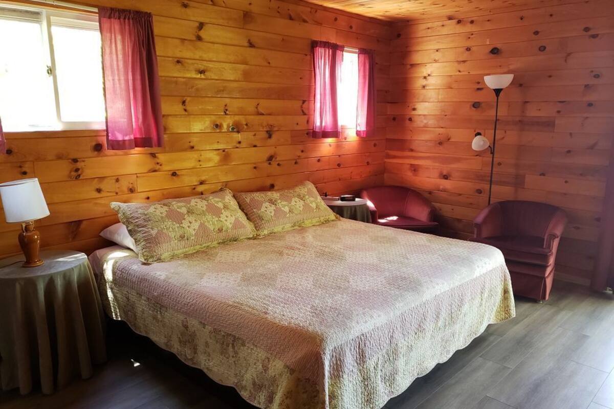 Une chambre confortable aménagée dans un chalet en bois, avec un grand lit, une table de chevet, une chaise et une lampe.