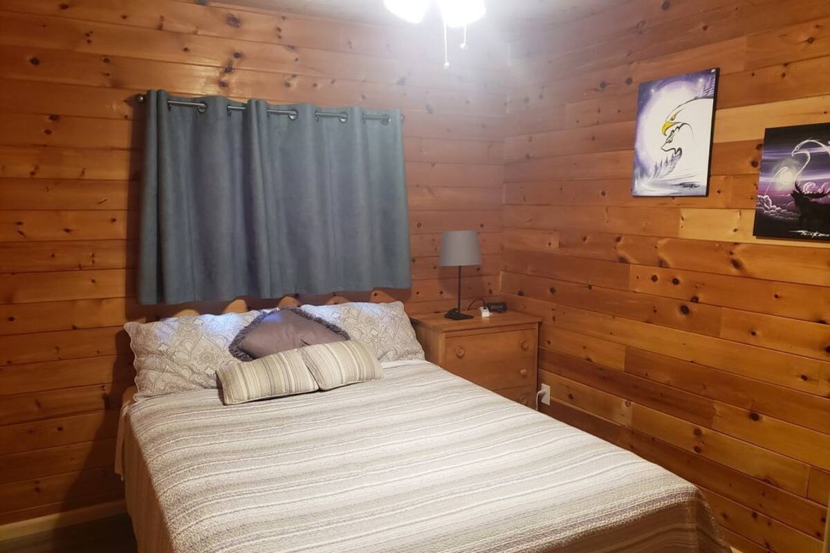Une pièce aux murs lambrés, comprenant un lit, une table de chevet, une lampe et deux œuvres d’art accrochées au mur.
