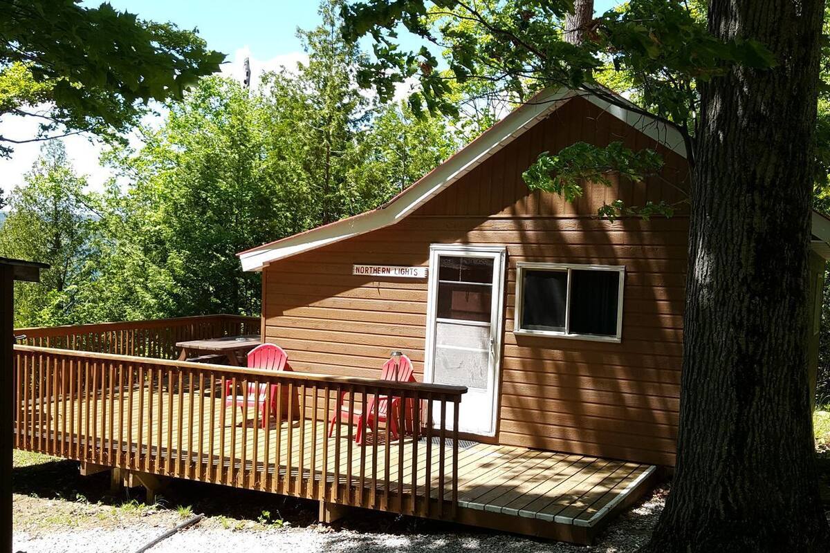 Une petite cabane en bois avec une porte, une fenêtre et une terrasse dotée de chaises rouges.