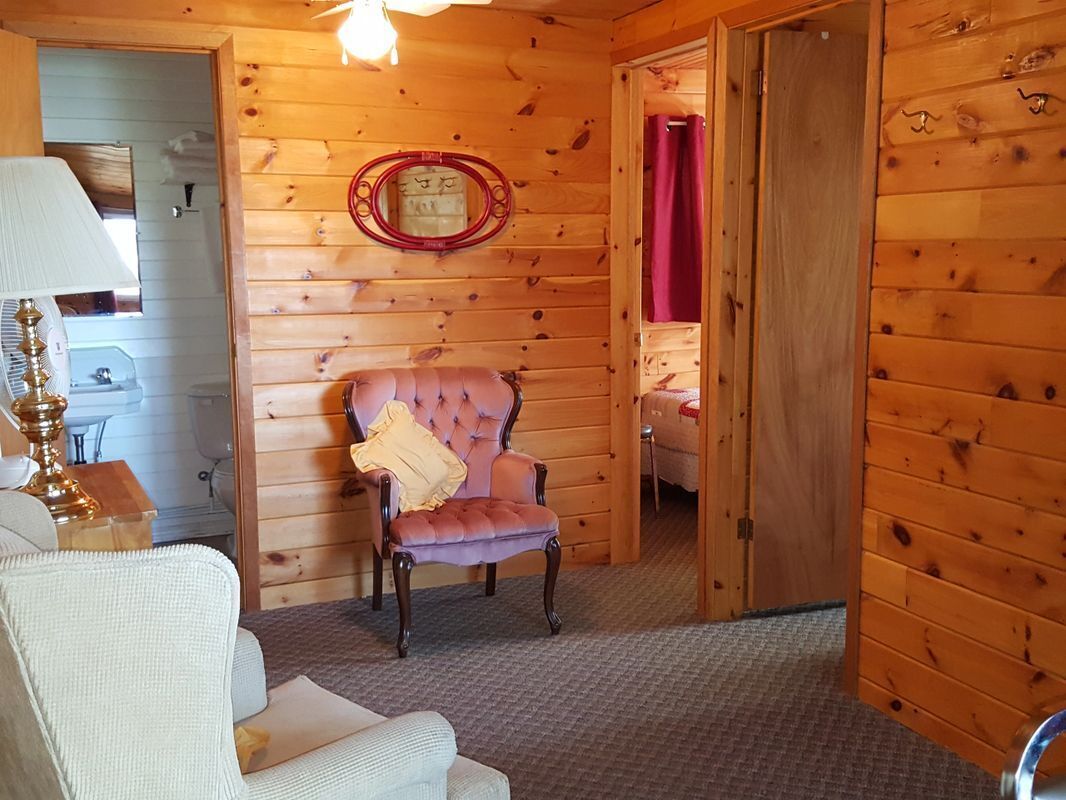 A log cabin room with a tufted armchair, a lamp, and a mirror on the wall.