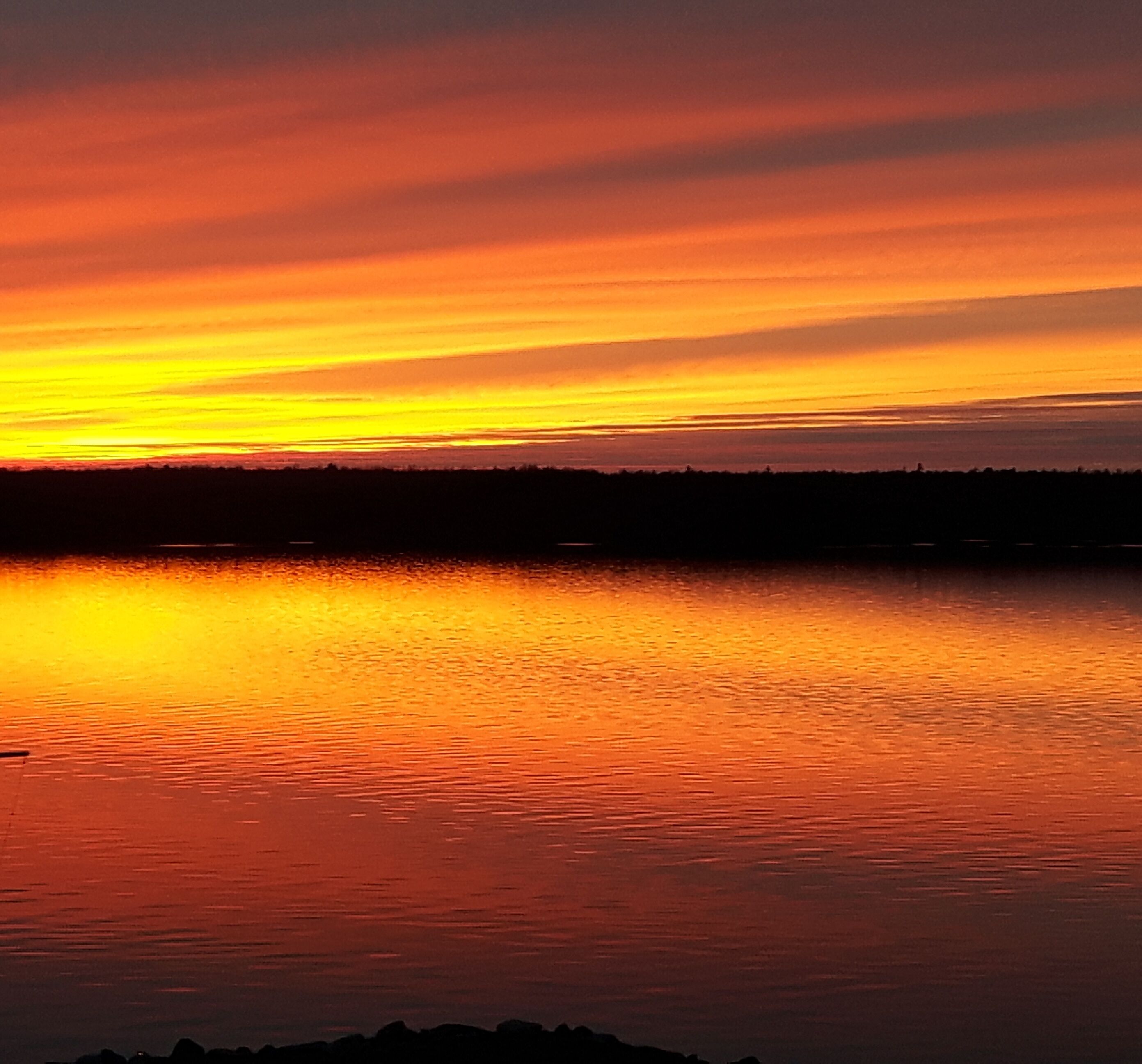 A sunset over a calm body of water with a silhouette of land in the distance.