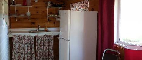 Una cocina compacta con paredes de madera, un refrigerador, un lavamanos y una ventana con cortina roja.