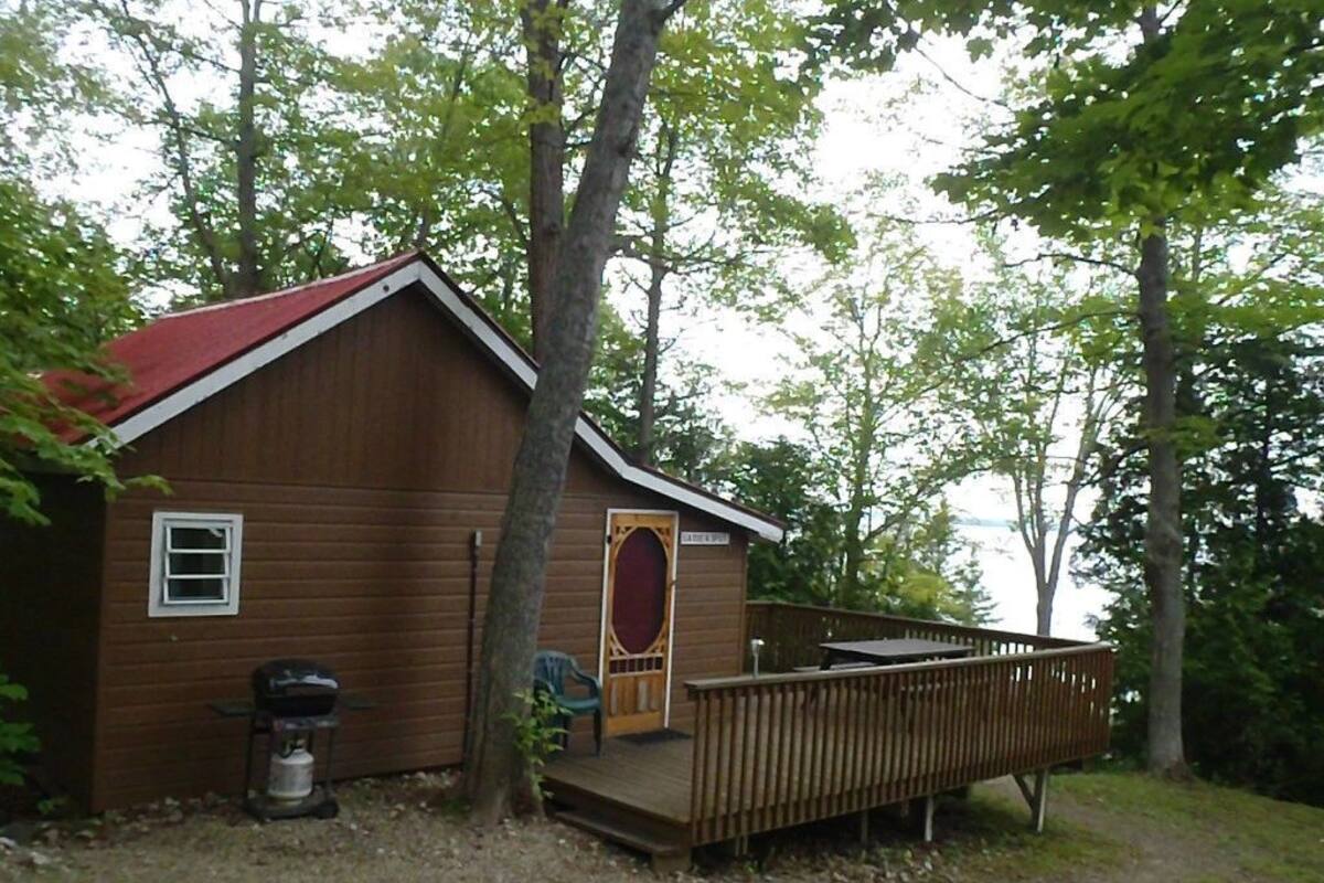 Une cabane en bois avec un toit rouge, une véranda et une vue sur un lac.