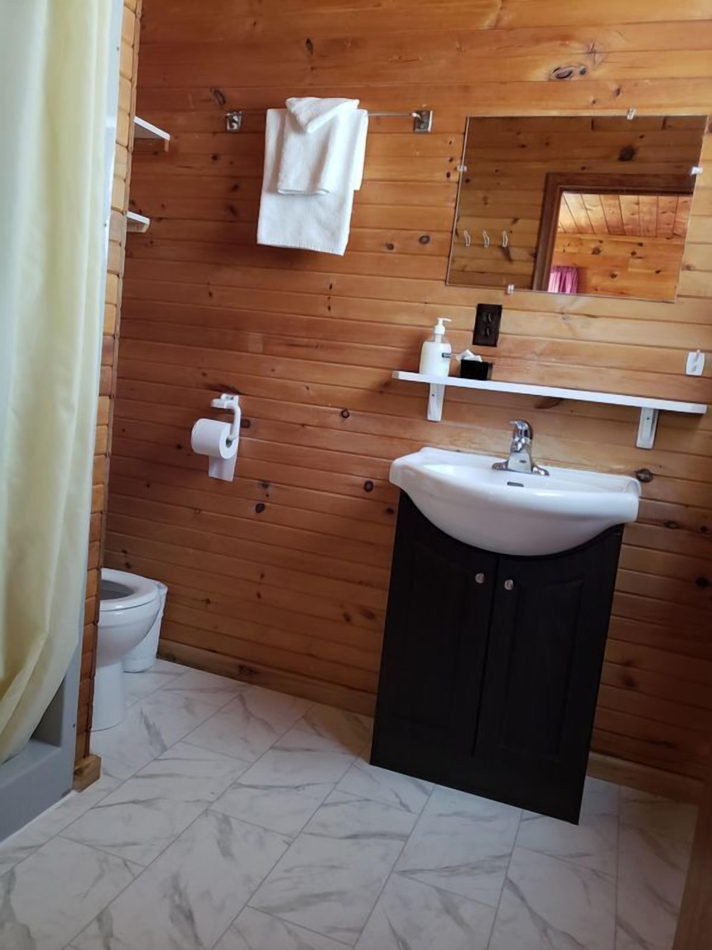 A bathroom with wooden walls, a white sink, a toilet, and a mirror.