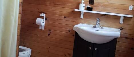 A bathroom with wooden walls, a white sink, a toilet, and a mirror.
