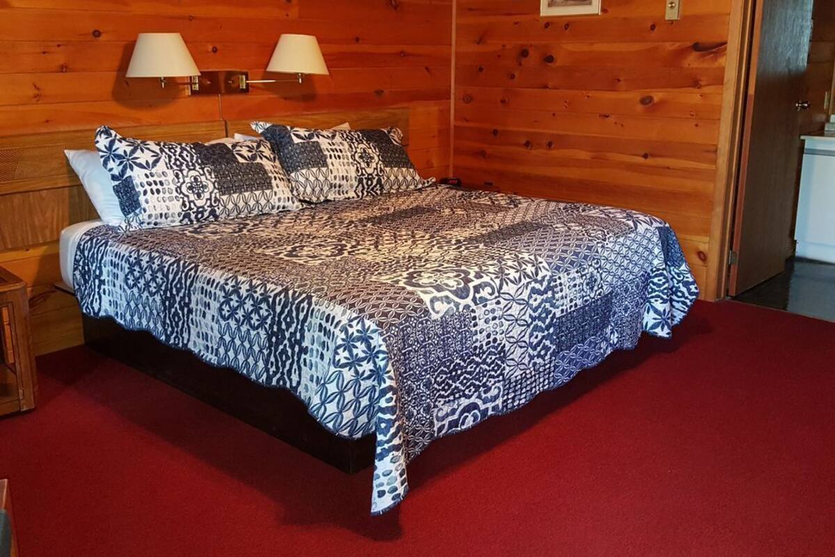 Une pièce de cabane en bois comprenant un lit, deux lampes fixées au mur et un tapis rouge.