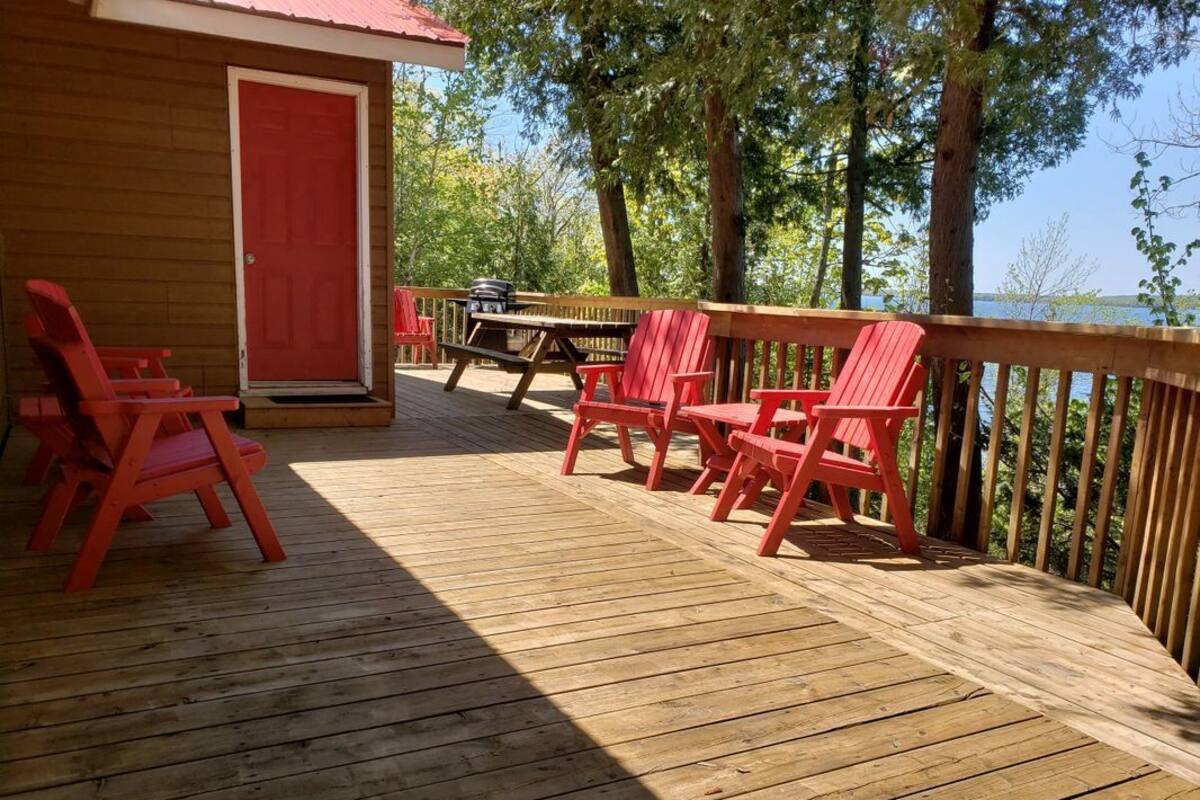 Une terrasse en bois avec des chaises rouges et une table, donnant sur une étendue d’eau.
