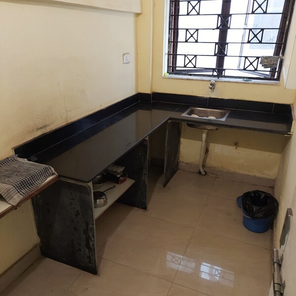 A small kitchen with a black countertop, a window with metal bars, a sink, and a blue trash bin.