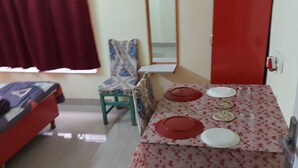 A dining area with a table set for four, a red door, a mirror, and a bed in the background. - Serene Peaceful Flat (Kolkata)