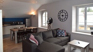 Un salon moderne avec un canapé gris, une petite table blanche et un coin repas comprenant une table et des chaises en bois.