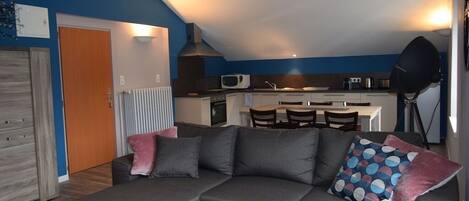 A modern living room with a grey sectional sofa, a wooden coffee table, and a kitchen in the background.