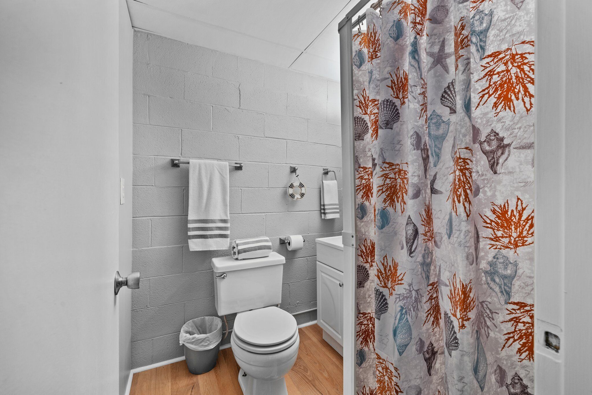 A bathroom with a white toilet, a sink, and a shower curtain with a sea shell pattern.