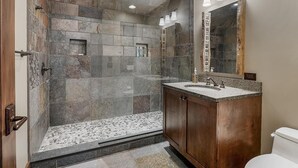 A modern bathroom with a stone shower enclosure, a wooden vanity, and a large mirror. - Lakewood Pointe and Guesthouse - Free Railroad Admission + Majestic Views + (Bryson City)