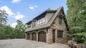 A two-story stone house with a gabled roof, multiple garage doors, and a driveway leading to a stone wall. - Lakewood Pointe and Guesthouse - Free Railroad Admission + Majestic Views + (Bryson City)