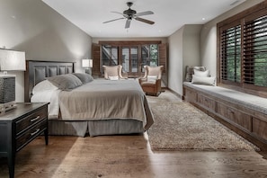 A bedroom with a large bed, a desk, two chairs, a ceiling fan, and a window with blinds. - 7BR lake-front luxury estate with hot tub, game room, and guesthouse. (Bryson City)