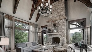 Ein geräumiges Wohnzimmer mit Kamin aus Stein, Ledersofas und großen Fenstern mit Blick ins Freie.