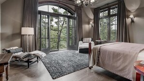 Ein großzügiges Schlafzimmer mit einem großen Bett, einer Liege und Blick ins Freie durch große Fenster.