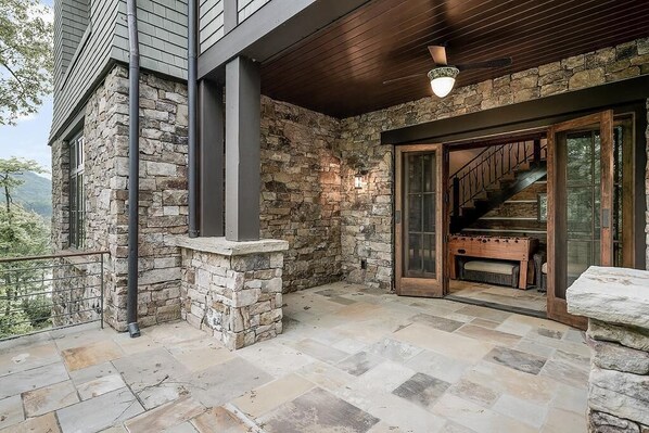 A stone exterior with a wooden deck, a staircase leading to a glass door, and a stone wall. - 5BR lakefront luxury estate with hot tub, game room, private dock (Bryson City)
