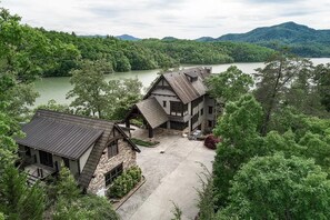 Uma pousada grande e rústica, com vários edifícios, rodeada por uma floresta densa e um lago.