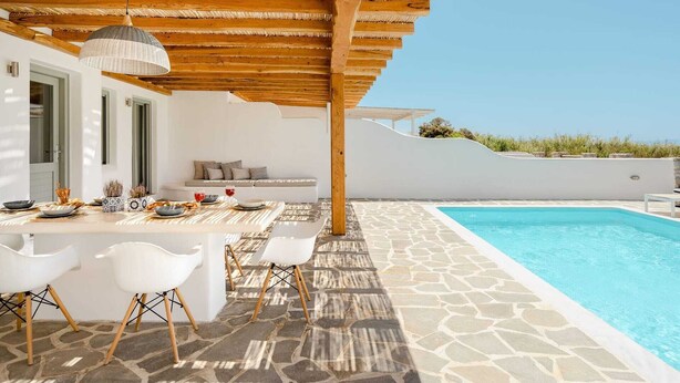 A poolside area with a stone floor, white furniture, and a wooden pergola.