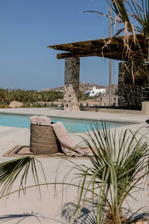 Ein Poolbereich mit Liegestuhl, einer Pergola und Blick auf ein weißes Gebäude im Hintergrund.