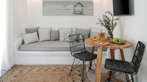 A modern living room with a sofa, two chairs, a wooden table, a woven rug, a wall-mounted TV, and a pendant light.